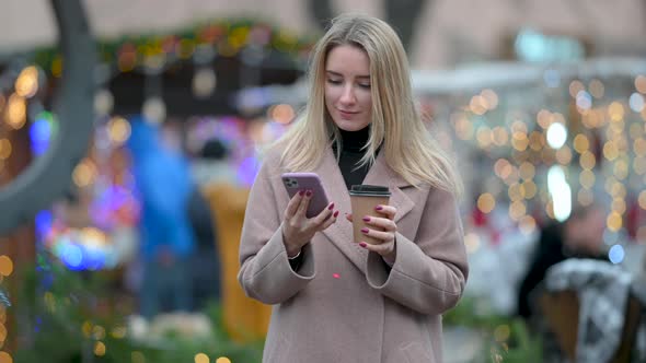 Young Lady with a Cup of Hot Coffee Using Mobile Phone alt