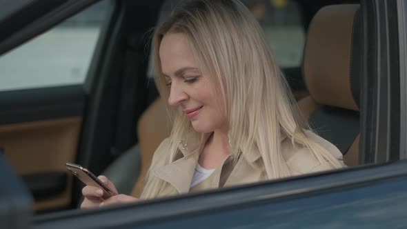 The Woman Driver Is Sitting Behind the Steering Wheel Reading a Text Message on a Mobile. The alt