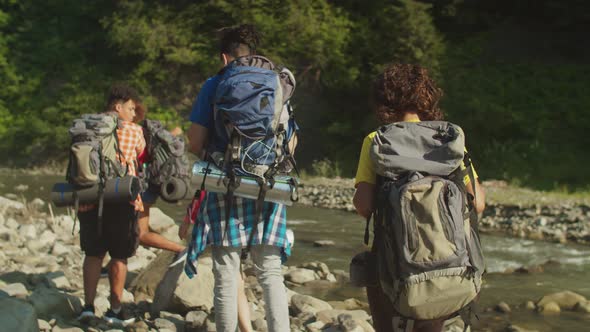 Rear View of Diverse Multiracial Tourists with Backpacks Backpacking By Mountain River alt