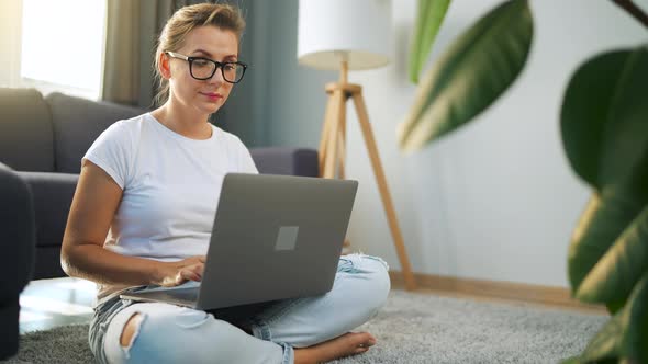 Woman with Glasses is Sitting on the Floor and Working on a Laptop alt