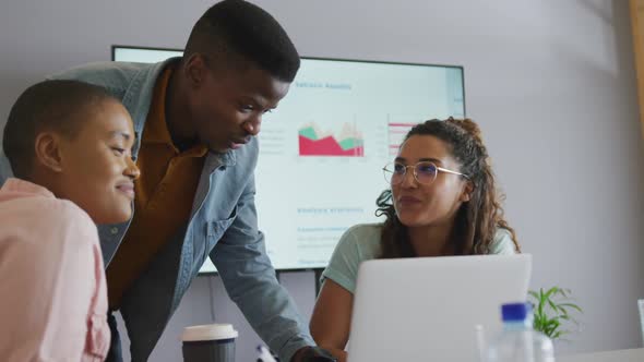 Three diverse creative male and female colleagues in discussion at meeting using laptop and screen alt