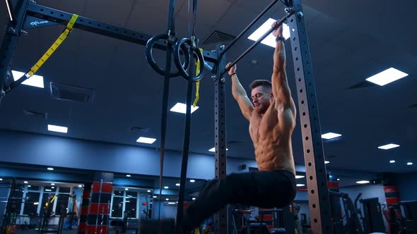 Bodybuilder exercising on horizontal bar. Shirtless man pulling up on horizontal bar in gym alt