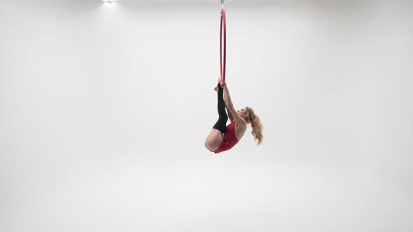 Gymnastics In A Red Dress Hanging On The Feet In The Air Ring alt