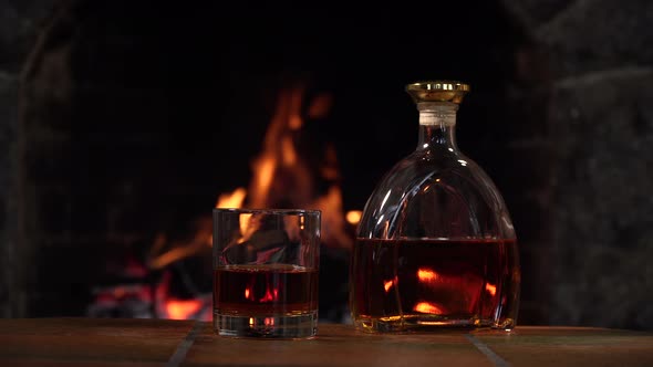 Bottle and Glass with Whiskey or Cognac on the Background of Fire in the Fireplace alt