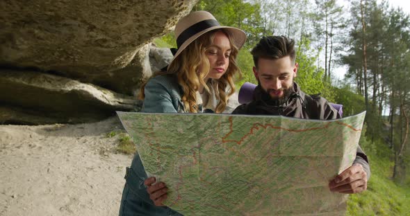A Guy and a Girl Are Standing Under a Rock and Looking for Interesting Places on the Map alt