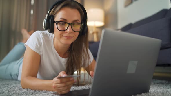 Woman with Glasses and Headphones Is Lying on the Carpet, Listening To Music alt