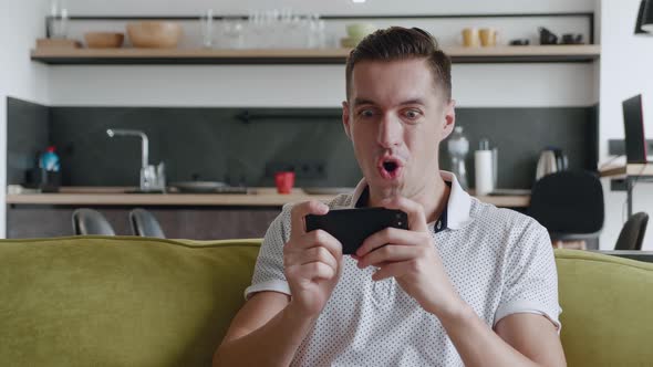 Young Man Playing on His Smartphone Exciting Mobile Application Winning a Racing Game Clenching Fist alt