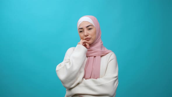Thoughtful Pretty Young Muslim Woman in Hijab Rubbing Her Chin and Looking Aside with Pensive