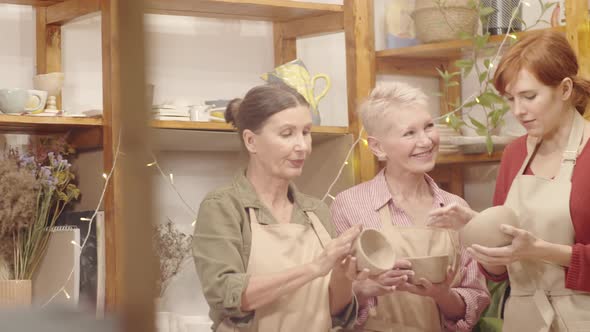 Experienced Female Potter Giving Advice to Elderly Crafters in Studio alt
