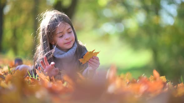 Cute little girl lies on the grass and collects a bouquet of leaves