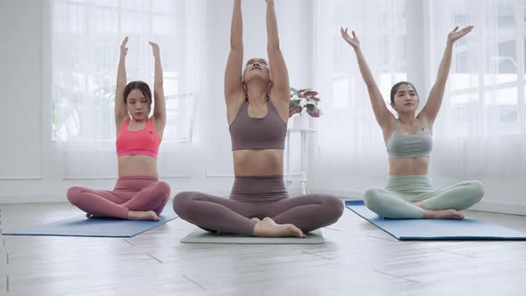 Asian female yoga teacher is teaching students in class basic exercises