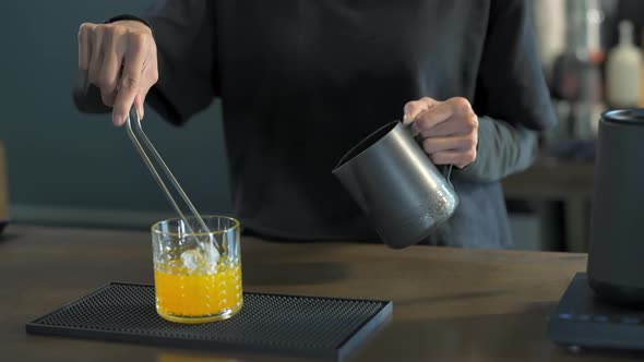 4K Asian woman barista making iced black coffee with orange juice serving to customer