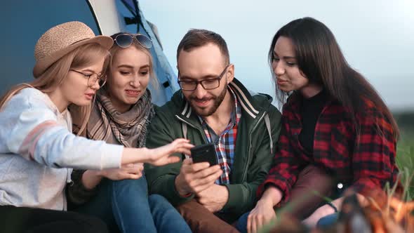 Guy and Girls Surfing Internet Holding Phone Sit Near Bonfire alt