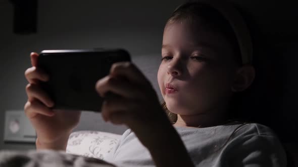 a Little Girl Watches Cartoons Plays Games on a Smartphone at Night in the Dark