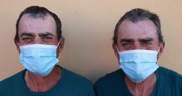 Senior twin men looking and smiling while wearing safety face masks for coronavirus outbreak alt