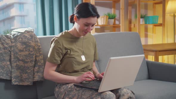 Young Smiling Military Woman Sits at Her Laptop alt