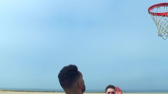 A man does a slam dunk while playing one-on-one basketball hoops on a beach court alt