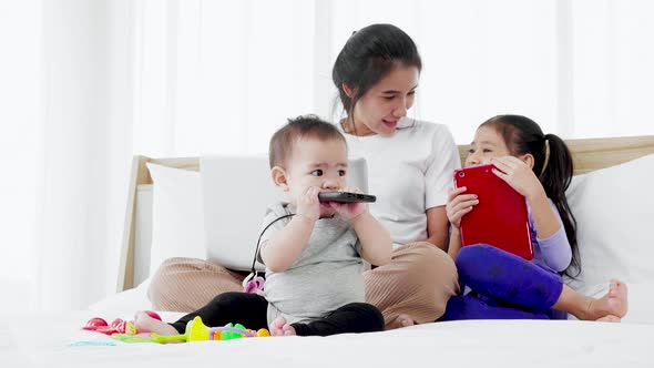 Mother of busy working on laptop computer, playing with baby and talking to little daughter