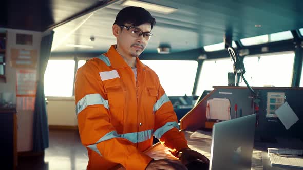 Filipino Deck Officer on Bridge of Vessel or Ship. He Is Using Laptop, Electronic Paperwork at Sea alt