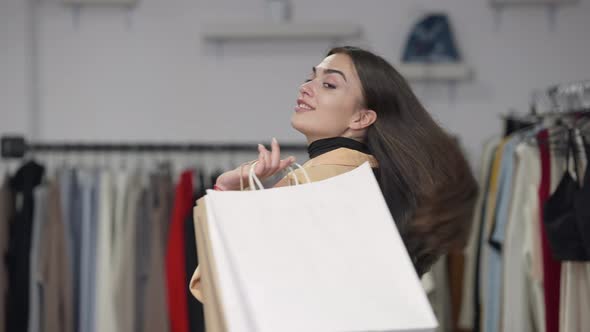 Beautiful Slim Caucasian Millennial Woman Turning Hanging Shopping Bags on Shoulder Looking at alt