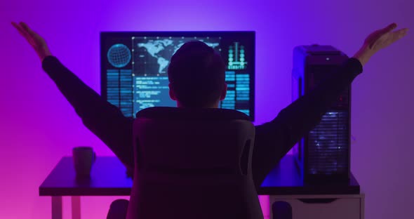 Rear View of Man Programmer Happy with Success While Working at a Computer in Data Center at Night alt