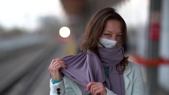 Woman with Facial Mask From Respiratory Infection and Scarf Is Standing on Railway Platform at alt