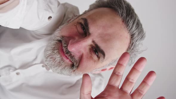 Vertical Studio Closeup Shot of a Content Happy Caucasian Bearded Man with Grayhair Waving at Camera alt