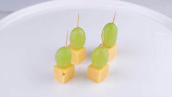 Rotating Cheese and Grape Canapes on White Plate or Background Closeupsnack Concept