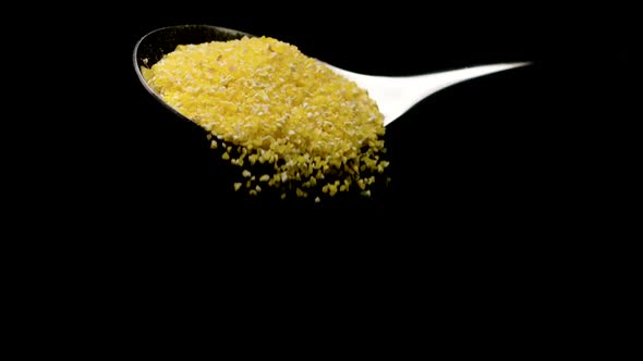 Organic Corn Grits Falling Down From Teaspoon Isolated on Black Slow Motion