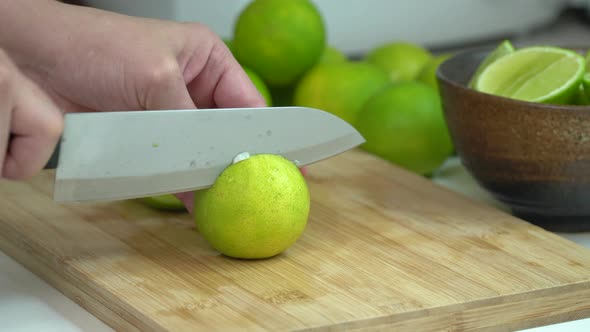Hand Slicing fresh Lime With Knife On Wooden Board In Kitchen alt