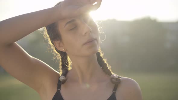 Close-up of Confident Tired Sportswoman Wiping Forehead with Hand at Sunrise. Portrait of Beautiful alt