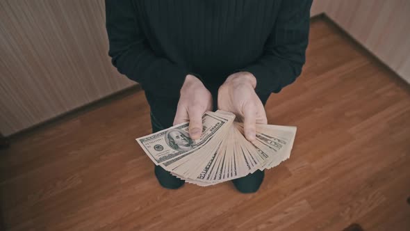 Young Man on His Knees Shows a Lot of Dollar Bills Spread Out Like a Fan alt