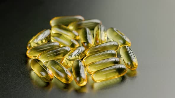 Group of Golden Transparent Pills with Liquid Medicine Rotating on Black Surface