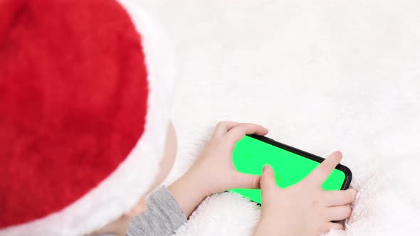 Kid preschool in Santa hat with gadget playing video games digital on mobile phone at home