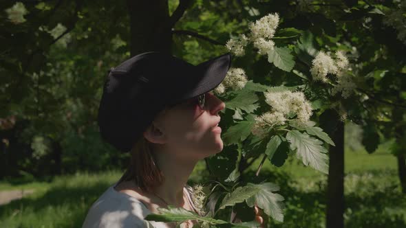 Young Woman Bends Over Tree Smells Aroma of White Flowers Sunny Summer Day alt