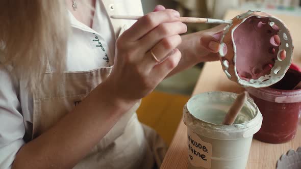 Close Up View of Female Potter Wearing Apron Using Glaze Brush to Paint on Pot alt