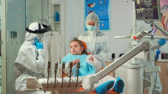 Orthodontist in Protection Coverall Speaking To Mother of Kid Patient alt