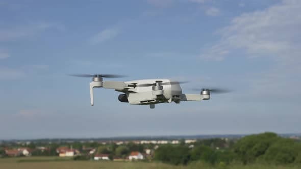 Quadcopter Consumer Drone Flying Slowly  Above Green Suburban Landscape on Sunny Day, Slow Motion alt