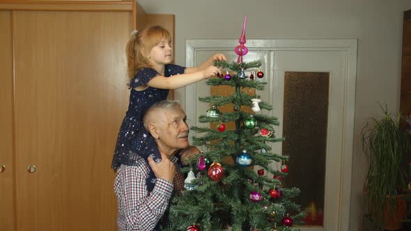 Little Child Girl with Senior Grandparent Decorating Artificial Christmas Tree at Oldfashion Home alt