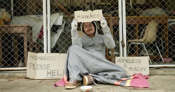 Homeless man holding homeless label and sitting on floor. alt