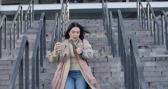 Portrait of Brunette Adult Woman Running Down the Stairs with Coffee Cup and Folder with Documents alt