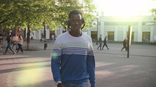 A Young Black Student with Headphones Walks Through the City Centre at Sunset