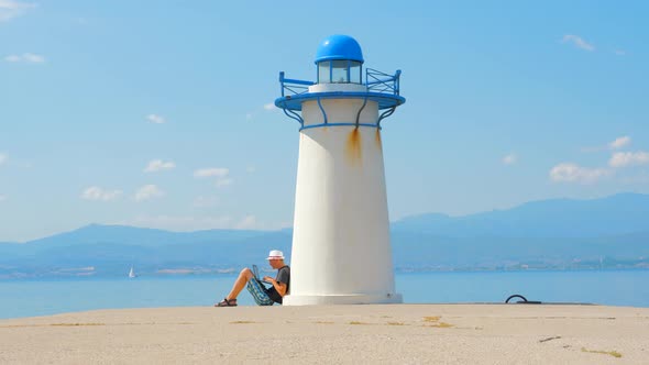 Freelancer Works on Seaside Near Lighthouse in Greece. Easy To Find a Job. Job Search Near the Sea