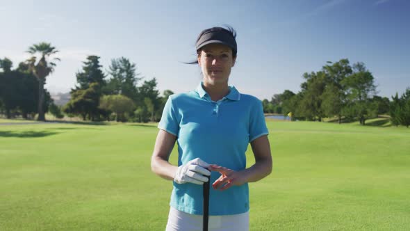 Portrait of female caucasian golf player smiling while standing with golf club at golf course alt