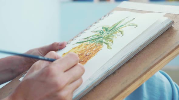 Closeup of Female Hand with Paintbrush is Drawing a Pineapple By Watercolors