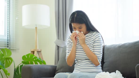 Asian beautiful woman having running nose and sneezing in living room. alt