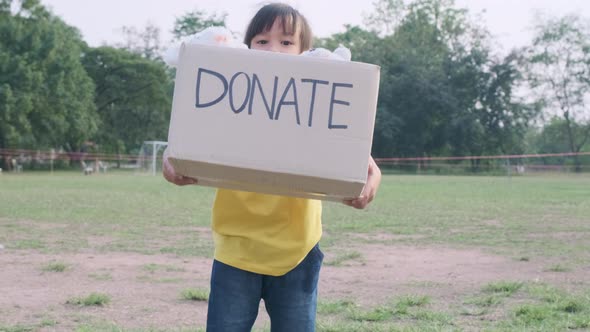 Cute little girl holding donation box with old dolls outdoors. Donation concept. alt