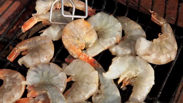 Top View of the Large Raw Shrimps Flipped on the Grill Grid with Kitchen Tongs alt