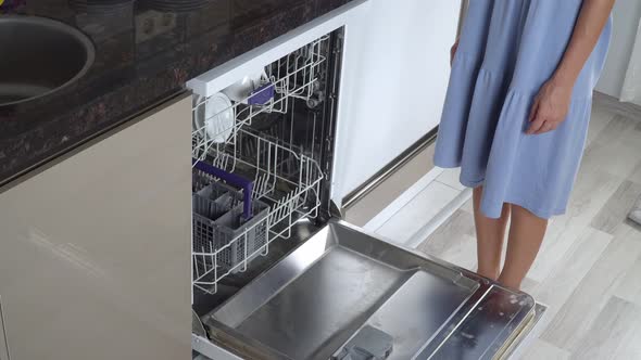 A Woman Pushes Out the Top Shelf of a Dishwasher with Clean Dishes