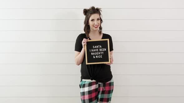 Woman holding sign saying, Santa I have been Naughty and Nice alt